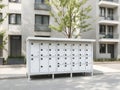 A row of white mailboxes are lined up on the sidewalk in front of a building Royalty Free Stock Photo