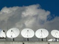 A row of white parabolic antennas look in the sky