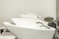 Row of white porcelain sinks for washing hair in a hair salon with taps and hoses Royalty Free Stock Photo