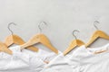 Row of white pure cotton wrinkly T-shirts hanging on wooden hangers on gray background. Casual unisex clothes natural materials