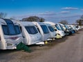 A row of white touring caravans on hardstanding in a secure caravan storage facility on a sunny day in winter