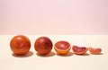 A row of whole and cut into halves and slices of blood oranges on a yellow-pink background in bright light Royalty Free Stock Photo