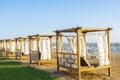 Row of wooden furniture for rest with curtains, deck chair bed, gazebo on sand beach with grass lawn, tropical sea Royalty Free Stock Photo