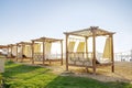 Row of wooden furniture for rest with curtains, deck chair bed, gazebo on sand beach with grass lawn, tropical sea luxury resort. Royalty Free Stock Photo