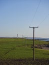 A row of wooden Telegraph poles crossing a field at Usan towards the Scurdie Ness lighthouse in the distance. Royalty Free Stock Photo