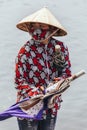 Rowing boat woman wearing red and white colors shirt, conical hat and mouth mask stand and carry umbrellas in Ninh Binh, Vietnam