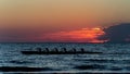 Rowing crew in silhouette on water against pastel sunset sky