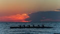 Rowing crew in silhouette on water against pastel sunset sky