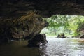 Rowing woman row a boat with tourist on the river inside cave with trees in the background at Trang An Grottoes in Ninh Binh.