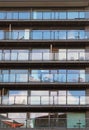 Rows of apartments in a large modern building with glass balconies and outdoor furniture and sky reflected in the windows Royalty Free Stock Photo
