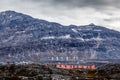 Rows of colorful modern Inuit houses among mossy stones with grey steep slopes of Little Malene mountain in Royalty Free Stock Photo