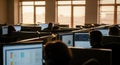 Rows of computer monitors glow in a sunlit classroom or office with natural light streaming in Royalty Free Stock Photo