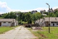 Rows of destroyed dilapidated hangars at abandoned military complex surrounded with pile of cut down trees and family houses