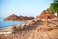 Rows of empty bamboo chaise lounge and thatched umbrellas on lonely white sand beach, on blue sea and green palm trees background