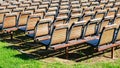 Rows of empty wooden chairs, lined up outside in the sun, on green grass. Concept for events, gatherings, shows