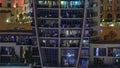 Rows of glowing windows with people in apartment building at night.