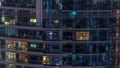 Rows of glowing windows with people in apartment building at night.