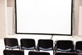 Rows of office chairs in front of a blank corporate multimedia presentation screen, vacant conference room interior, empty Royalty Free Stock Photo