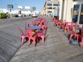 Rows of round cafe tables with salmon colored chairs on the boardwalk in front of a restaurant