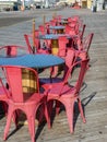 Rows of round cafe tables with salmon colored chairs on the boardwalk in front of a restaurant