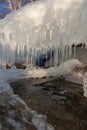 Rows of stalactite icicles hang from the stone. Icicles on the lake beach on the background of blue water