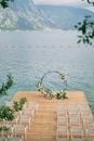 Rows of white chairs stand on the pier in front of a round wedding arch