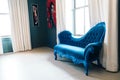 Royal blue vintage Victorian couch in a bright room with big windows, paintings and white curtains