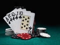 Royal flush standing leaning on chips piles on green cover of playing table. Black background. Close-up.