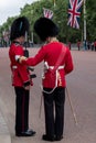 Royal Guard soldier in red and black uniform with bearskin hat stands to attention while colleague inspects him. The Mall, London Royalty Free Stock Photo