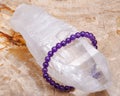 Royal purple Amethyst bead bracelet wrapped around Lemurian rainbow quartz point from Brazil on Natural Polished Petrified wood