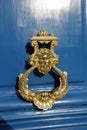 Royal style golden doorknocker on blue wooden door. face