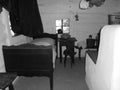 Retro image - Old wooden bed with chairs and table in a historic house next to white oven. Pillow and textile hanging from ceiling