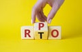 RPO vs RTO symbol. Businessman hand turns wooden cubes and changes the word RTO to RPO. Beautiful yellow background. business