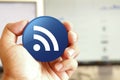 RSS icon blue round button holding by hand infront of workspace background Royalty Free Stock Photo