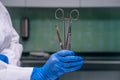 A rubber gloved hand holds two scalpels and a clamp