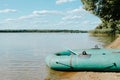 Rubber inflatable boat with paddle on shore of lake on sunny summer day outdoors, side view. Clouds and forest landscape Royalty Free Stock Photo