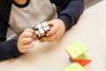 Rubik`s cube in children`s hands, closeup, white wooden background. Boy holding Rubik`s cube and playing with it