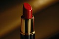 Ruby red lipstick on golden background. Beauty makeup cosmetics for lips. Glamourous fashion tube.