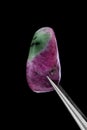 Ruby zoisite stone texture in tweezers on black background. Macro closeup Royalty Free Stock Photo