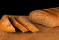 Ruddy loaf of bread and slices cut from it on a wooden board on a black background Royalty Free Stock Photo