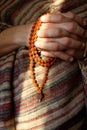 Rudraksha beads in men`s hands in traditional indian shawl. Man counting religious beads in sunlight.