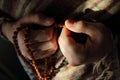 Rudraksha beads in men`s hands in traditional indian shawl. Man counting religious beads in sunlight.