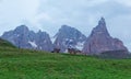 Rugged Cimon della Pala among peaks of Pale di San Martino mountains with a hotel on green grassy hill in Passo Rolle