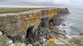 Rugged cliff face with sea caves and a sandy beach below, under a cloudy sky Royalty Free Stock Photo