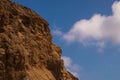 Rugged jagged brown cliff edge with a seagull on a ledge. Deep blue sky background with broken puffy clouds