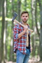Rugged look. Unshaven man carry axe in woods. Lumberjack style. Axeman wear open plaid shirt with jeans. Casual style