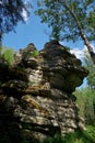 Rugged rock formations tower within a forest, their layered contours highlighted by sunlight filtering through the trees