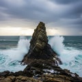 A rugged, triangular rock formation juts prominently from the ocean, with powerful Royalty Free Stock Photo