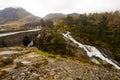 Rugged Welsh landscape, with a road and bridge over fast flowing river, rugged rocks, fir trees and low cloud ov er the mountains Royalty Free Stock Photo