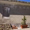 A ruined concrete building with a bricked-up window next to some bricks and plants in the courtyard Marche, Italy Royalty Free Stock Photo